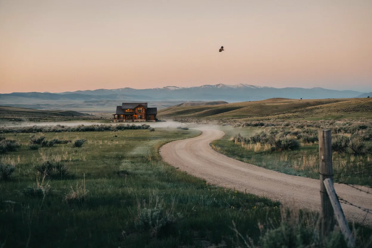 A lit cabin at dusk beside a winding road through the Colorado high country