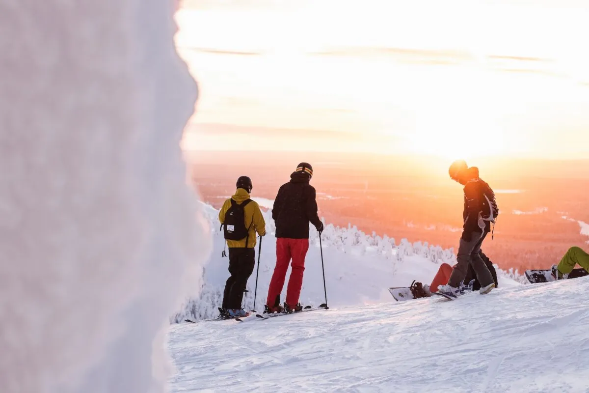Men on a snowy summit at sunset with skis and snowboards