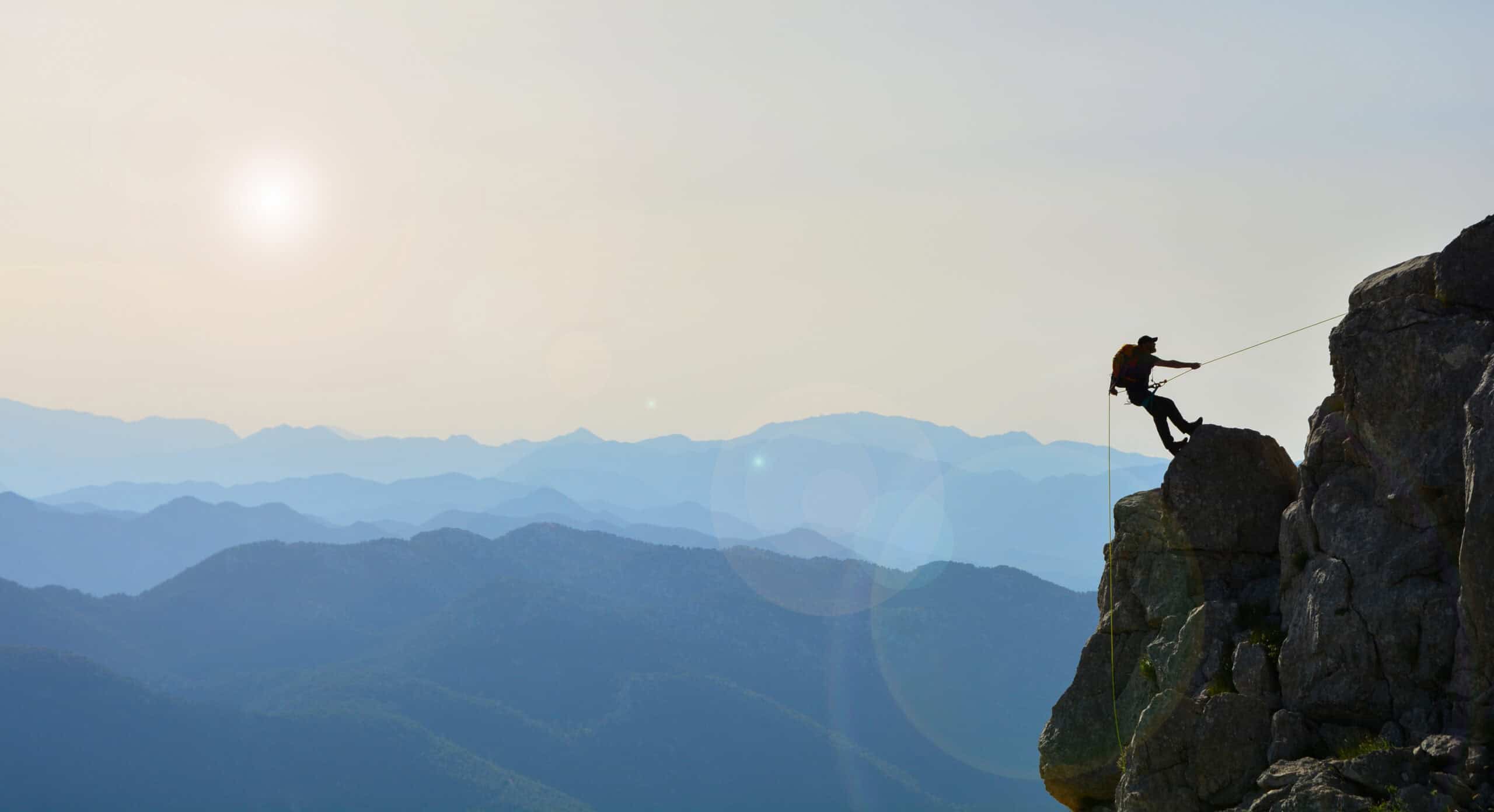 A climber rappelling down a cliff face above a mountain range.